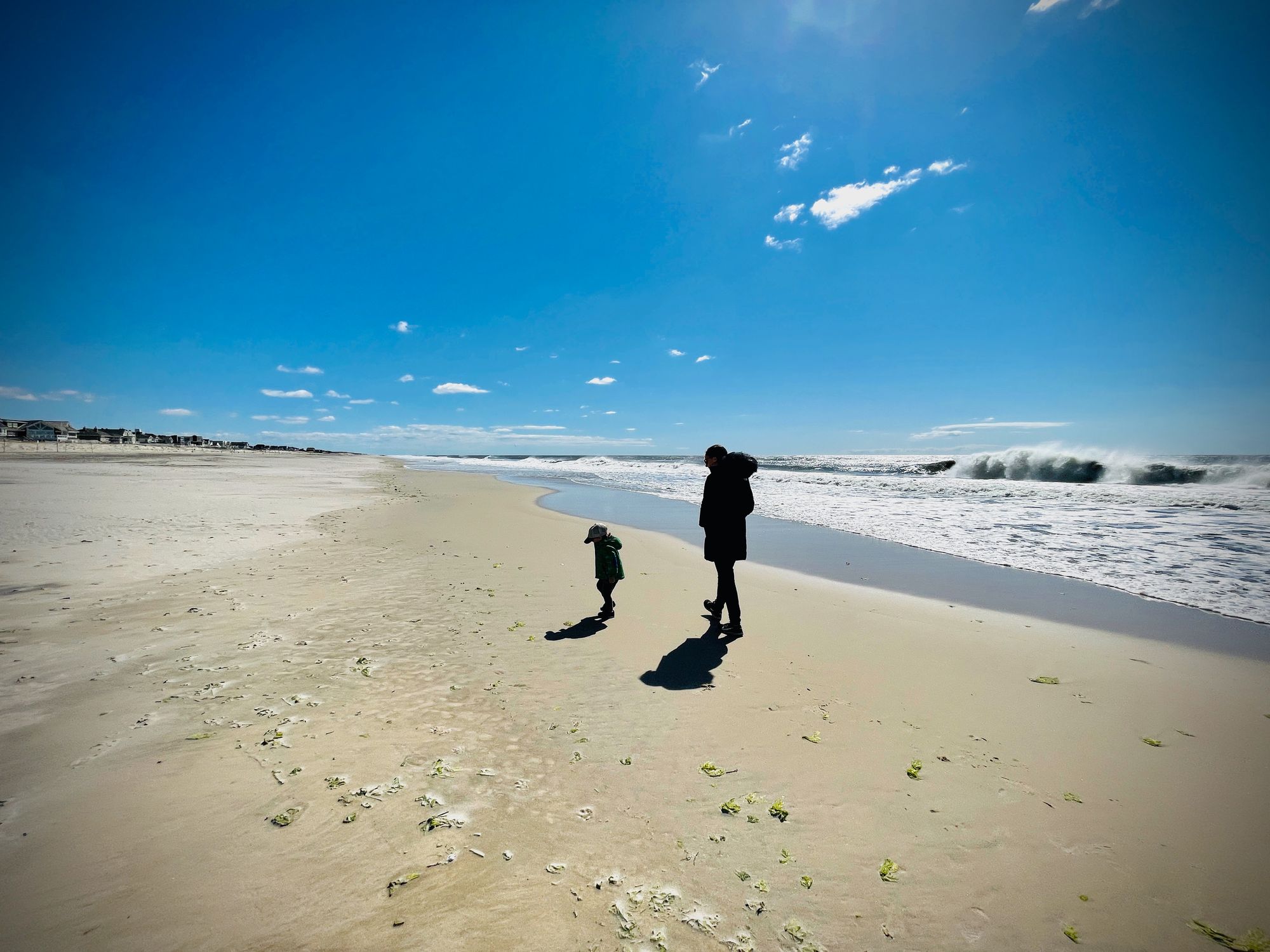 Two people, one child and one adult, walking on the beach.